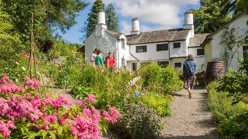 A group of four people walking in a garden front of a traditional farmhouse